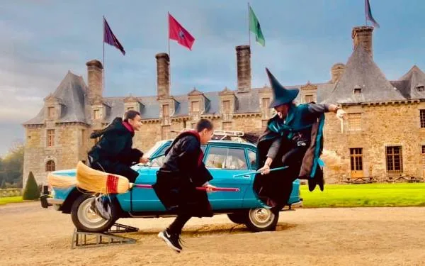 Image of the new wizarding school - Le Rocher Portail - with apprentice wizards and their teacher learning to tame their flying broomsticks! We can see in the background the blue car, the castle and the flags of the families.