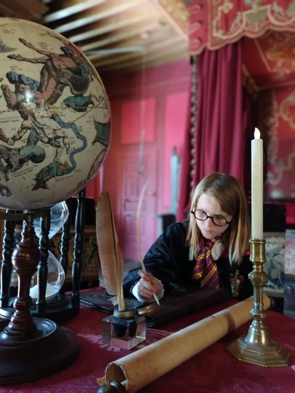 Image d'une enfant qui écrit à la plume au sein des décors enchantés de la nouvelle école des sorciers - Le Rocher Portail