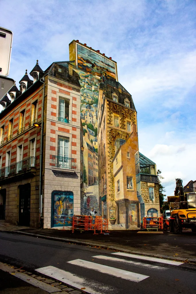 photo de rue, d'une grande fresque sur tout le long d'un immeuble. La fresque représente u trompe l'oeil comme si au travers de l'immeuble il y avait une autre rue et des habitants dessinés